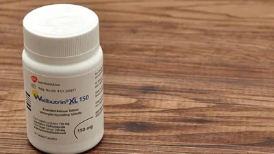 A bottle of Wellbutrin XL 150 mg extended-release tablets on a wooden surface, known to cause weight loss.